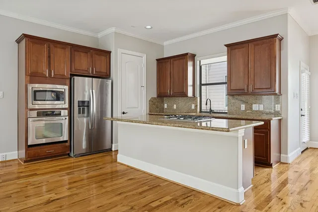a kitchen with stainless steel appliances granite countertop a refrigerator a stove and a sink with wooden cabinets