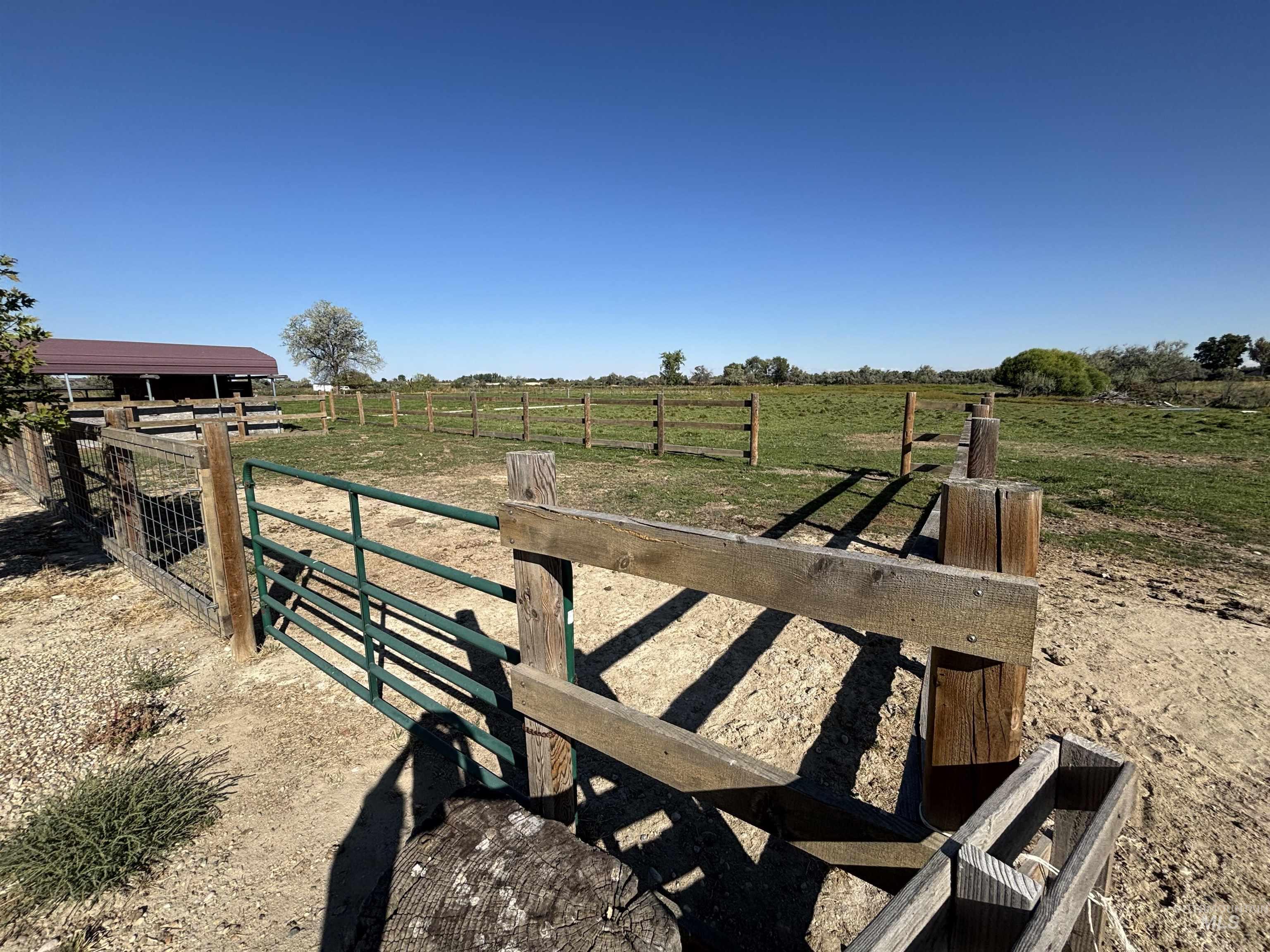 23626 Boise River Road Caldwell, ID 83607 - Photo 35 of 49 Expansive fenced pasture with a metal barn structure, multiple wood fence lines, and clear blue sky