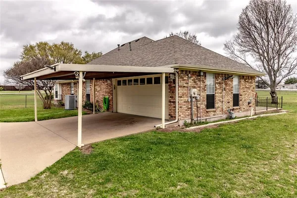 a view of a white house in front of a big yard plants and large trees