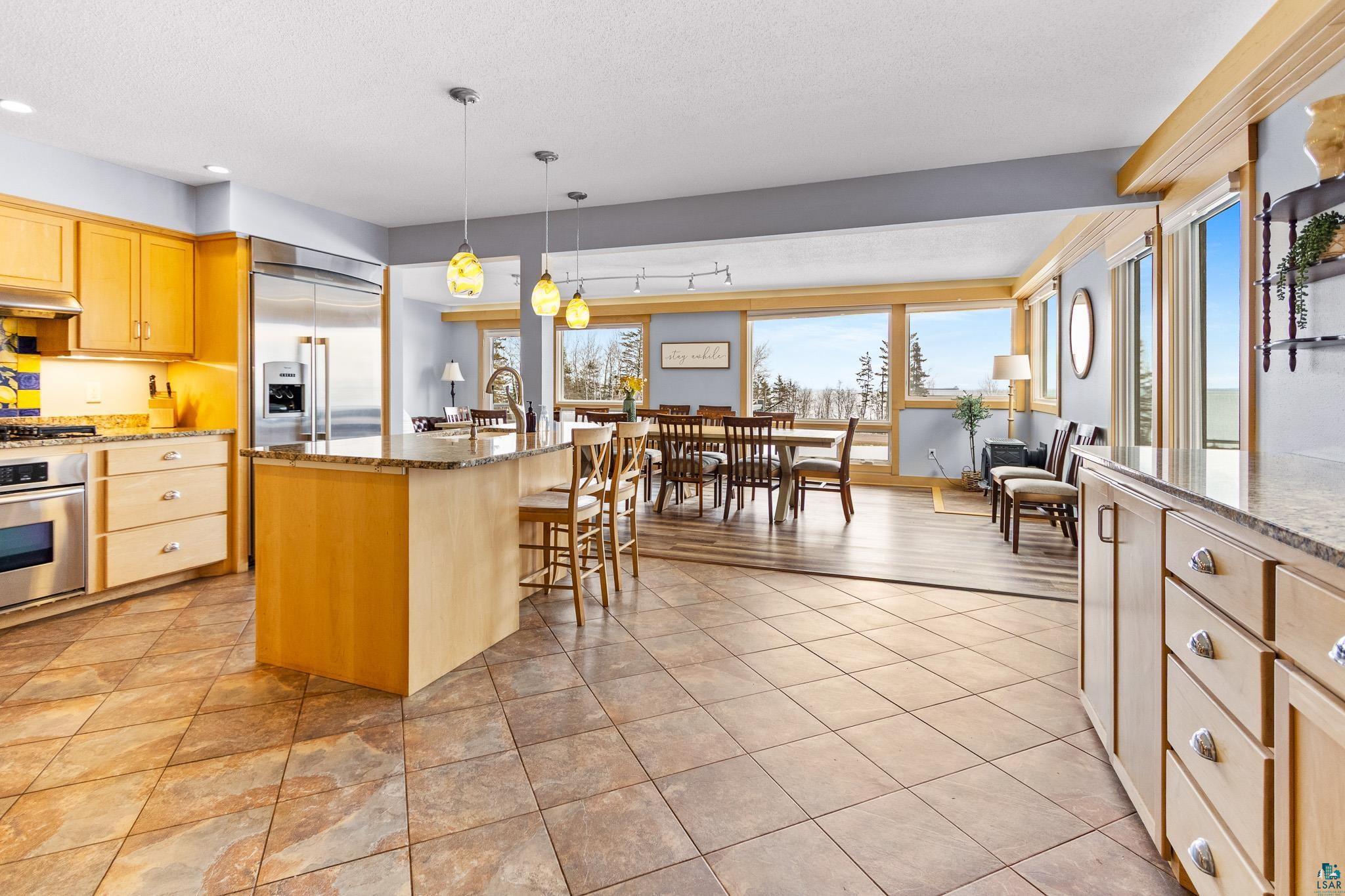 5163 Greenwood Road Duluth, MN 55804 - Photo 11 of 47 Open-concept kitchen and dining area featuring tile flooring, light wood cabinetry, stainless steel appliances, a kitchen island with pendant lighting, and large windows