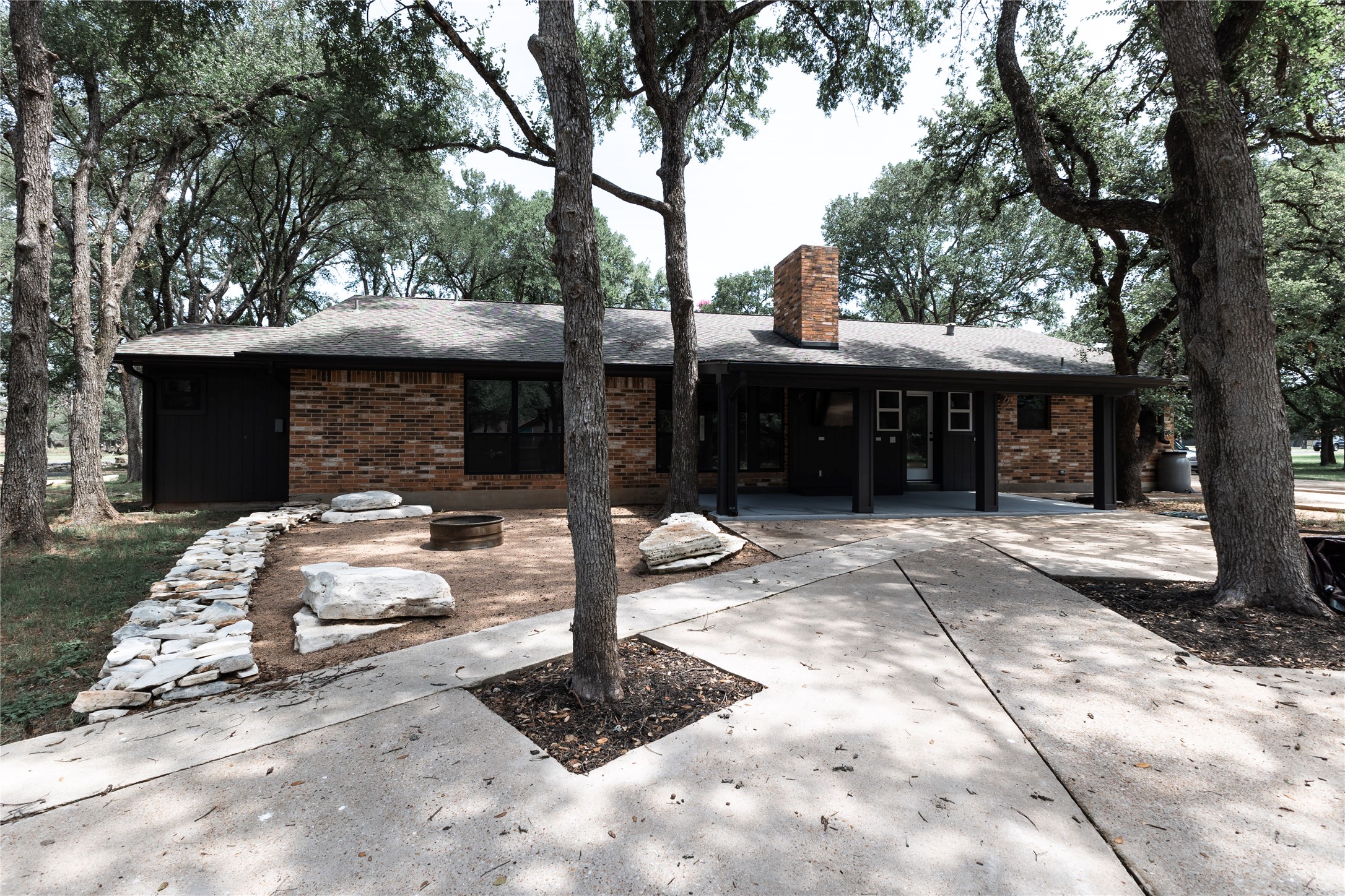 205 Bello Circle Georgetown, TX 78628 - Photo 36 of 36 Mature trees frame a charming brick exterior with a welcoming concrete pathway and stone landscaping.
