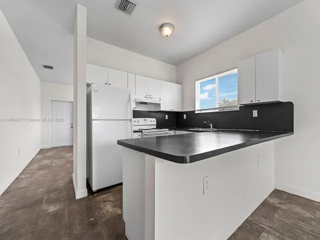 a kitchen with granite countertop a sink a refrigerator a counter top space and cabinets