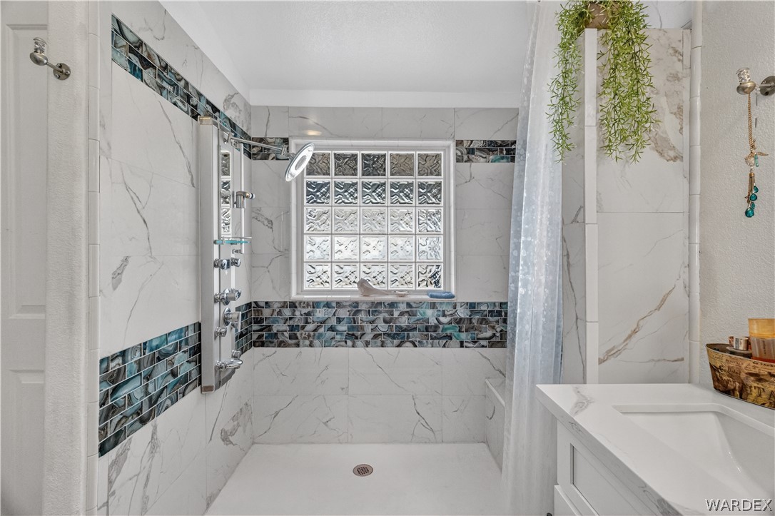 784 Pegasus Ranch Road Bullhead City, AZ 86429 - Photo 31 of 100 Walk-in shower with a glass block window, white and gray veined tile, and a blue-toned mosaic accent band