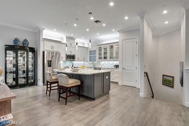 9637 Montelanico Loop, Unit 203 Naples, FL 34119 - Photo 4 of 50 Featuring a large island with seating, hanging pending light fixtures, stainless steel appliances, and cabs with glass fronts and open staircase