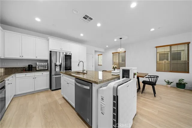 a kitchen with stainless steel appliances granite countertop a stove a sink a refrigerator and white cabinets with wooden floor