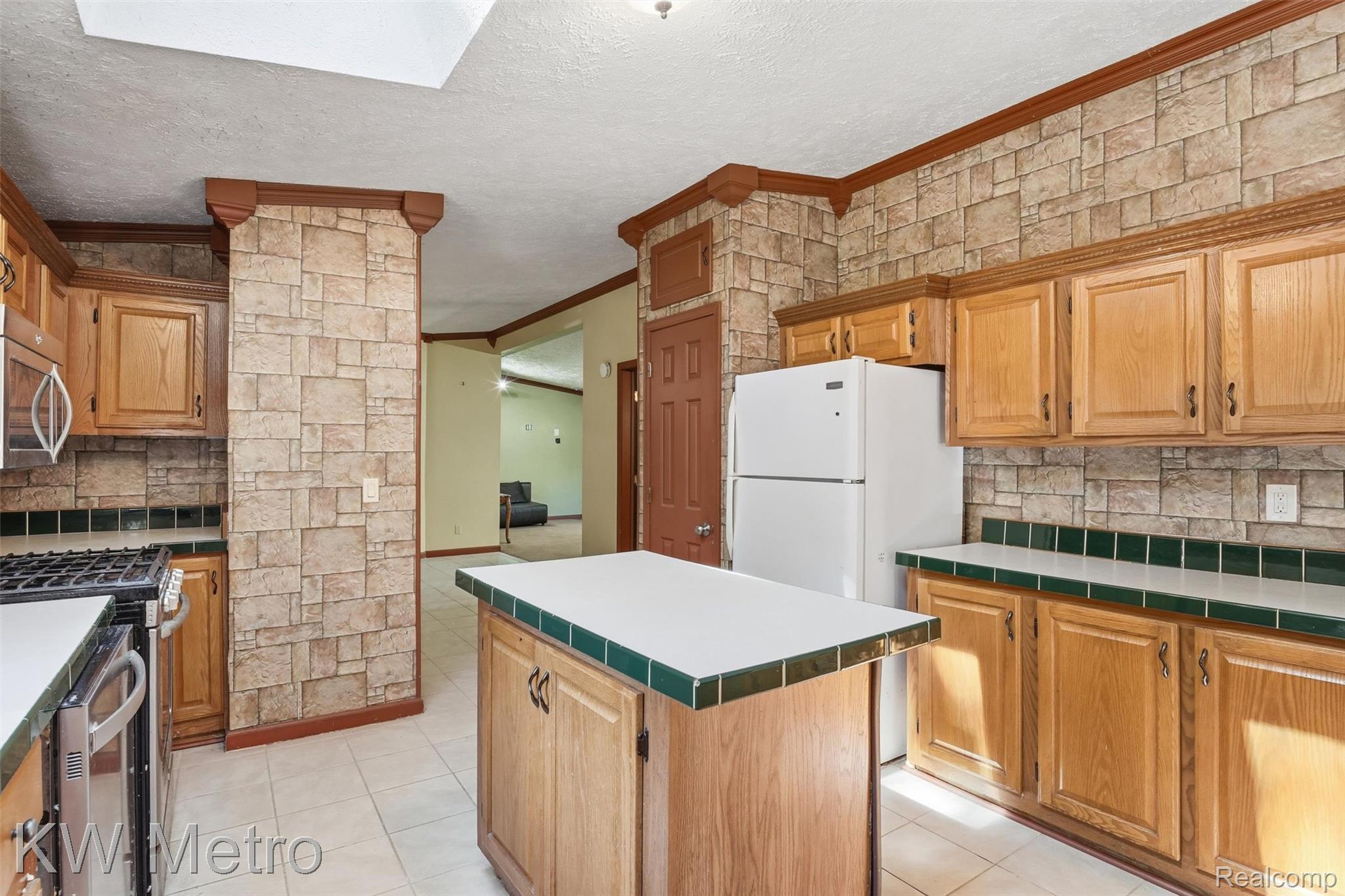 22733 Sumpter Road Belleville, MI 48111 - Photo 20 of 52 Kitchen featuring a central island with a white countertop and green tile trim, light wood-finish cabinetry, stainless steel range, and stone-look wall covering