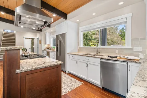 a kitchen with stainless steel appliances granite countertop a refrigerator a sink dishwasher a stove and white countertops with wooden floor