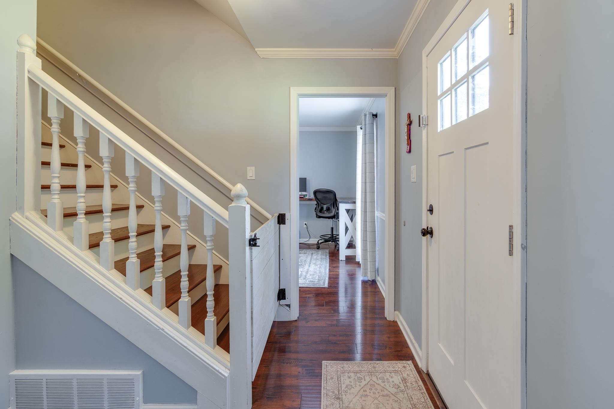 Entryway featuring wood-finish flooring, a paneled front door with glass lites, a white baluster staircase with wood treads, and crown molding