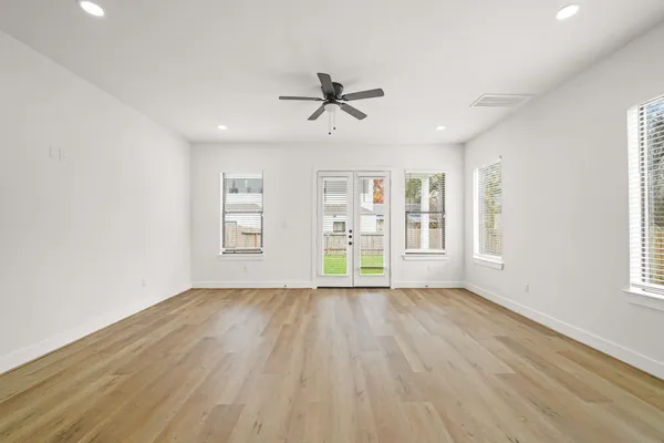 an empty room with wooden floor windows and ceiling fan