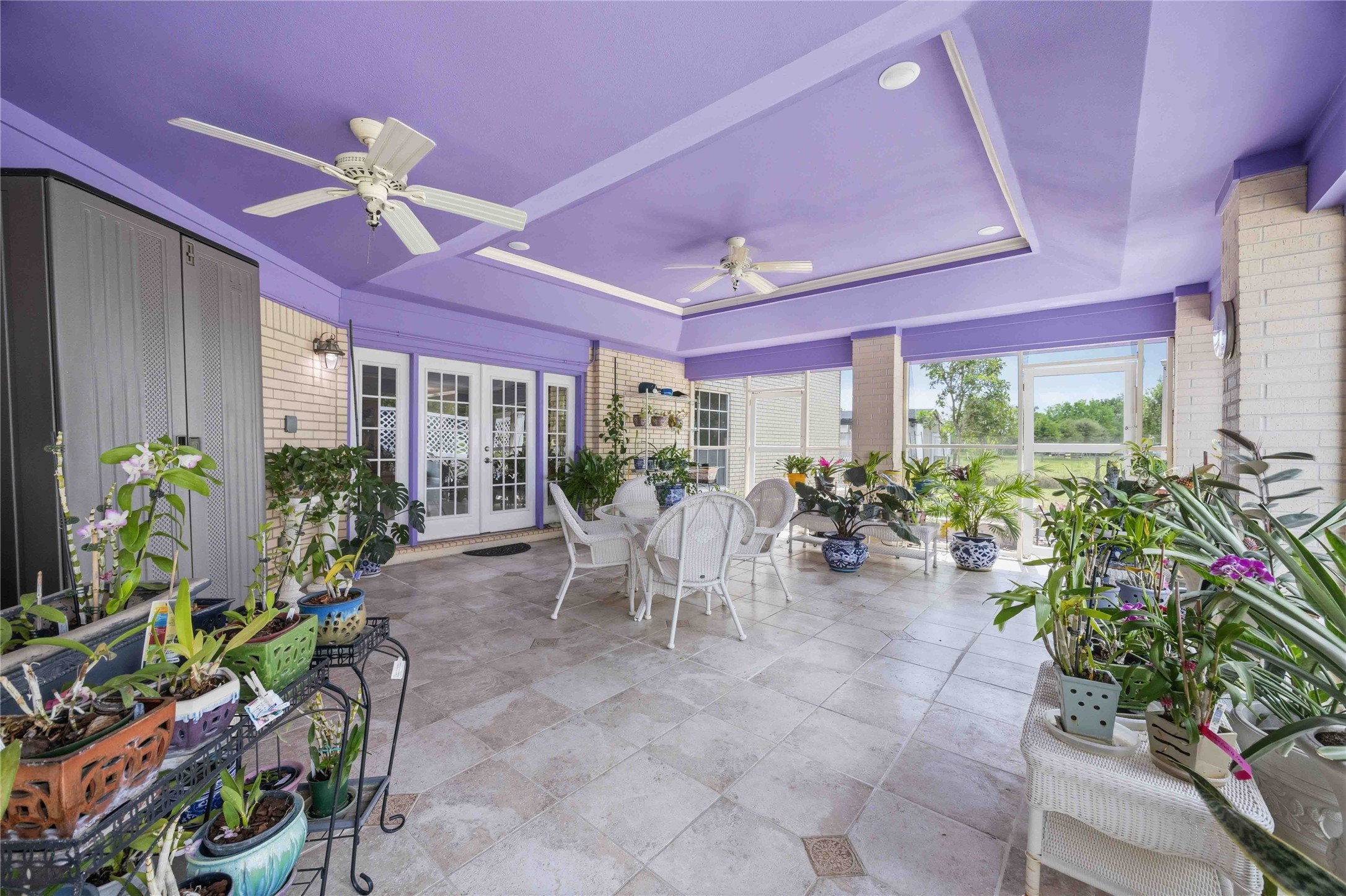 12075 Farm To Market 359 Hempstead, TX 77445 - Photo 3 of 46 This spacious sunroom features a vibrant purple ceiling, large windows for natural light, and tile flooring. It's decorated with abundant plants and includes ceiling fans and comfortable seating, offering a perfect space for relaxation and entertaining.