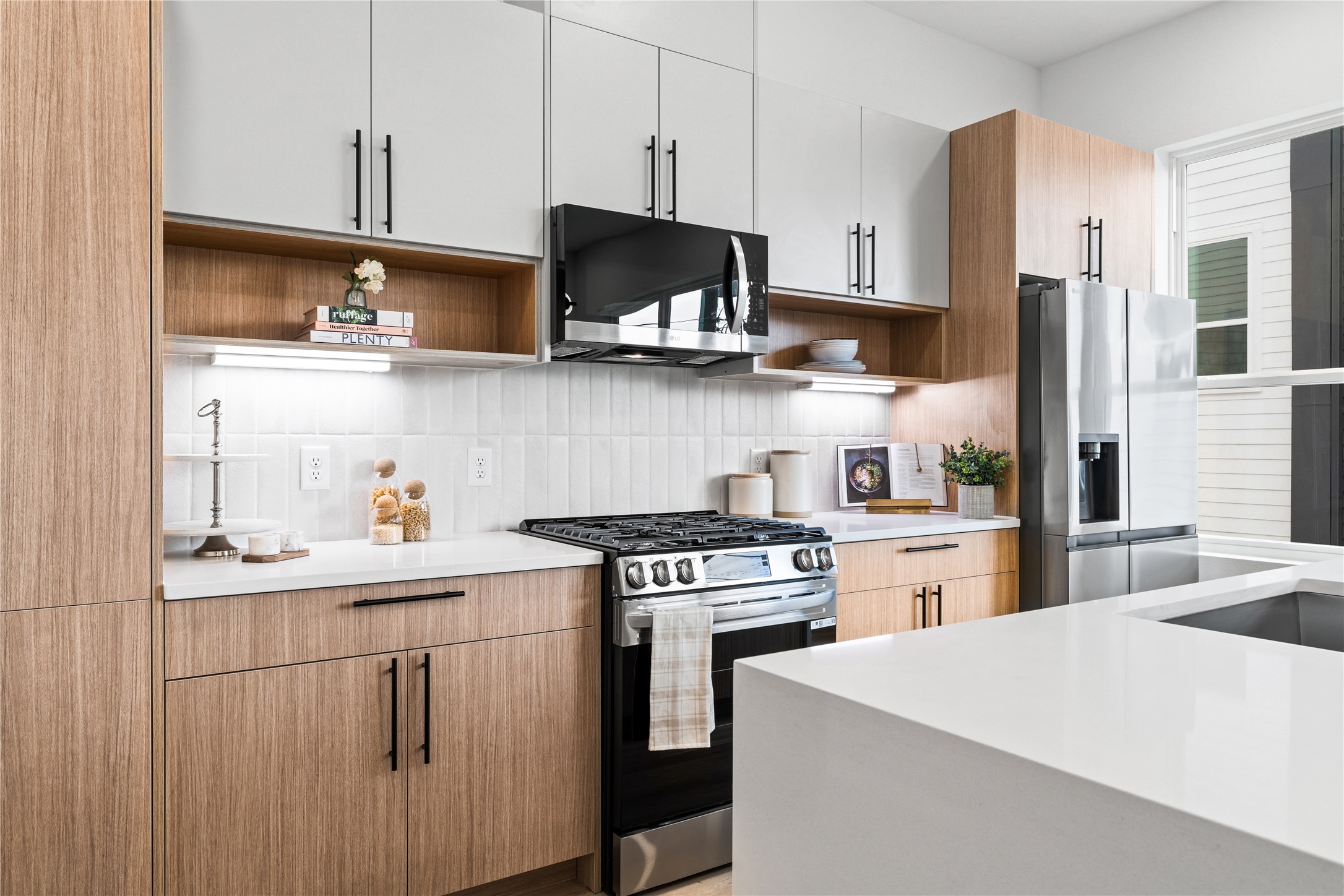 2948 Pitzlin Street Houston, TX 77023 - Photo 15 of 37 Every detail in this kitchen is designed to inspire—from the sleek gas range and built-in microwave to the wood-grain cabinetry with open shelving and soft-close drawers. The vertical tile backsplash adds subtle texture, while the oversized quartz island invites connection, creativity, and comfort in the heart of the home.
