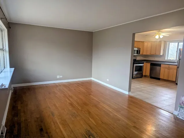 a view of an empty room and kitchen with wooden floor