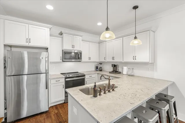 a kitchen with a sink a refrigerator a stove and white cabinets with wooden floor