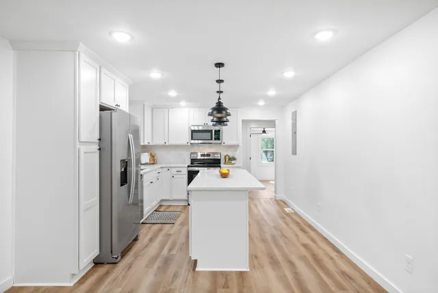 a kitchen with stainless steel appliances a refrigerator oven a sink dishwasher and white cabinets with wooden floor