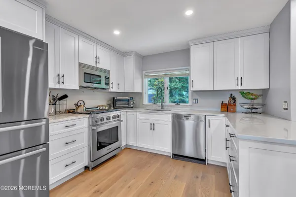 a kitchen with white cabinets appliances a sink and a window