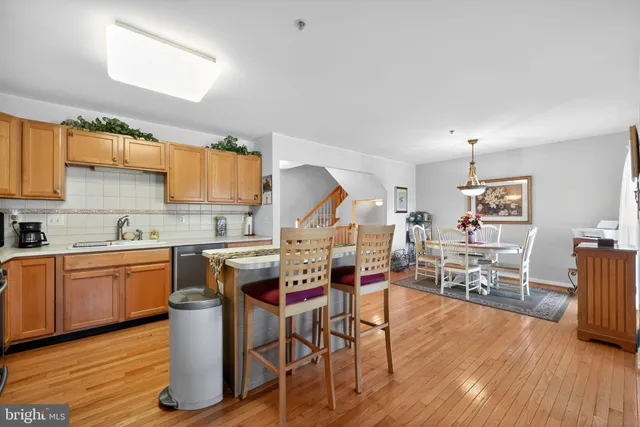 a open kitchen with stainless steel appliances granite countertop a stove top oven a sink dishwasher white cabinets with a dining table and chairs with wooden floor