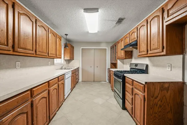a kitchen with stainless steel appliances granite countertop a stove top oven a refrigerator a sink and dishwasher with wooden cabinets