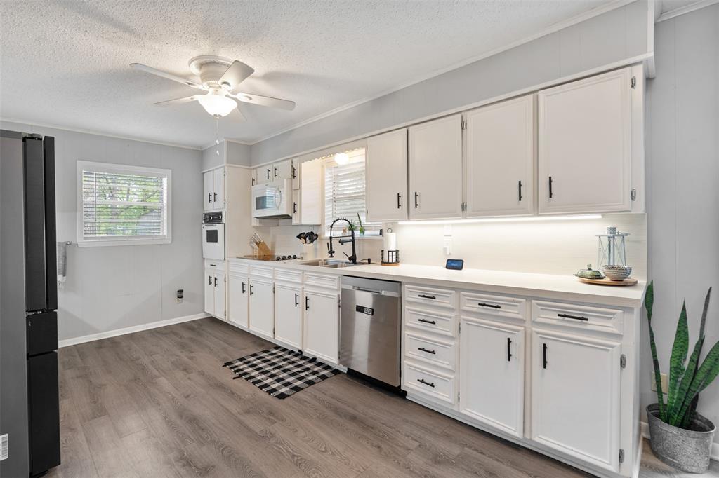 529 East Kempner Street Mabank, TX 75147 - Photo 4 of 16 a kitchen with white cabinets a sink dishwasher and a stove with wooden floor