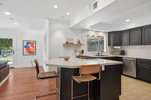 a kitchen with stainless steel appliances granite countertop a stove a sink a refrigerator and a dining table with wooden floor