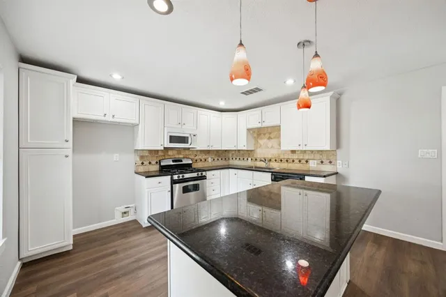 a kitchen with stainless steel appliances granite countertop a sink a stove and a wooden floor