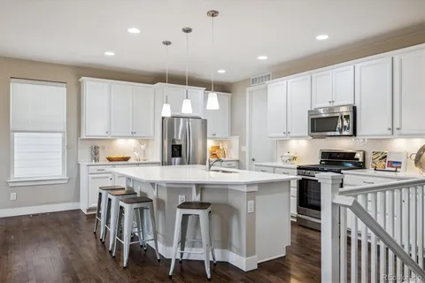 a kitchen with kitchen island granite countertop a sink a stove a refrigerator cabinets and chairs
