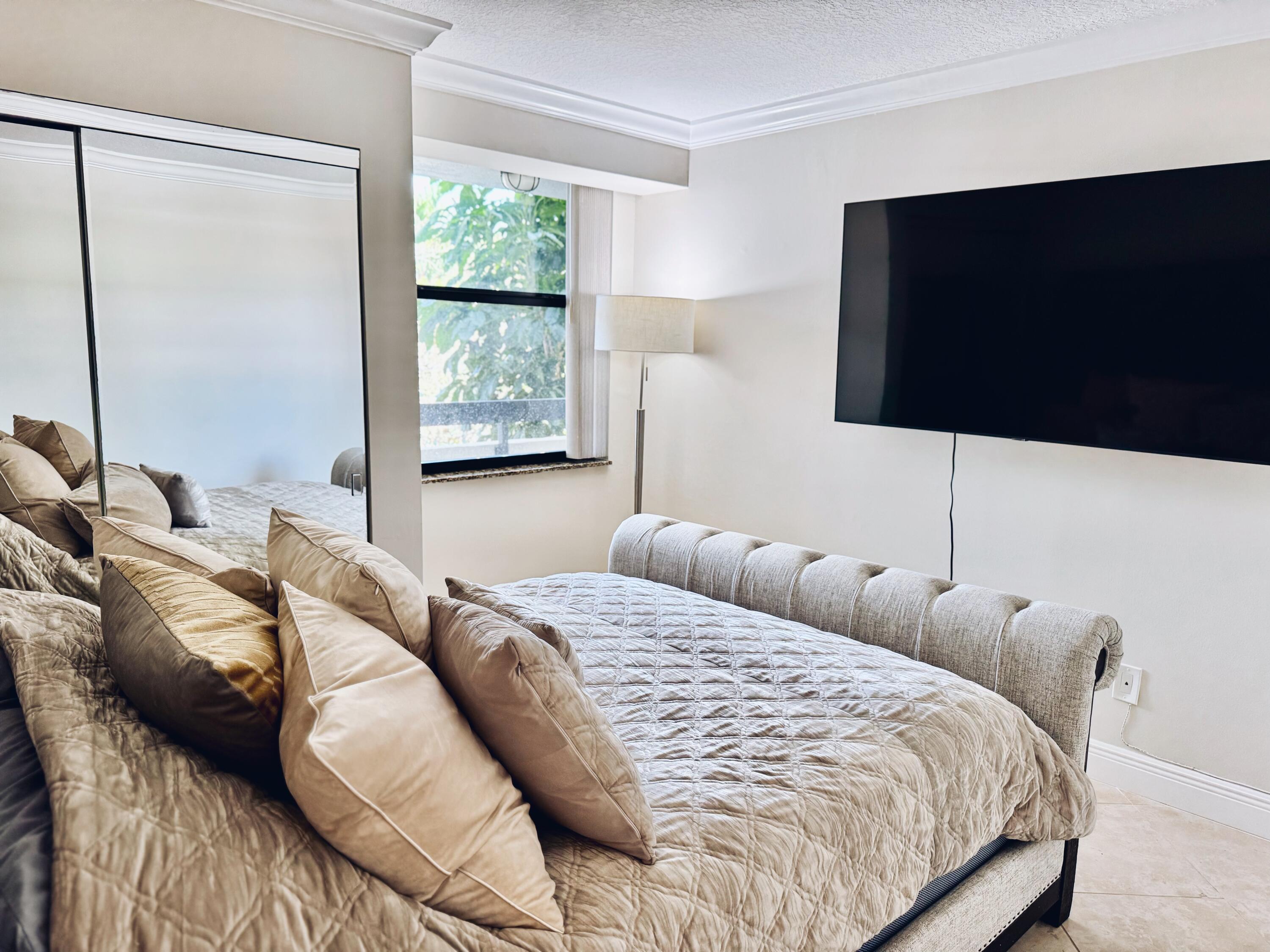 1915 Lavers Circle, Unit E209 Delray Beach, FL 33444 - Photo 17 of 20 a bedroom with a bed tv and window