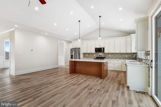 a kitchen with stainless steel appliances granite countertop a refrigerator a stove a sink and white cabinets with wooden floor