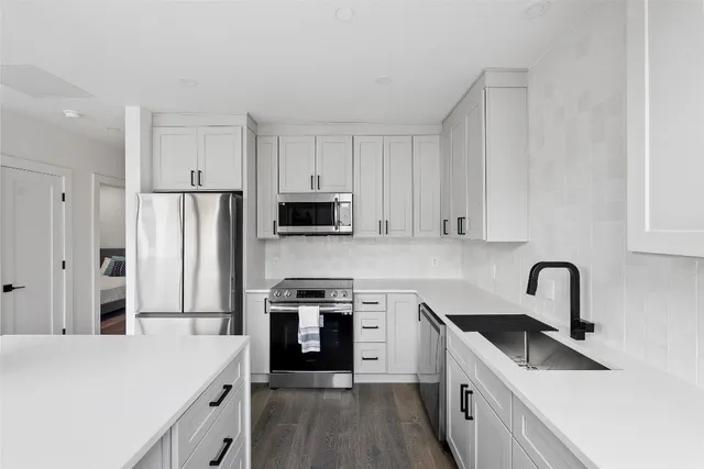 a kitchen with stainless steel appliances granite countertop a sink stove a refrigerator and white cabinets with wooden floor