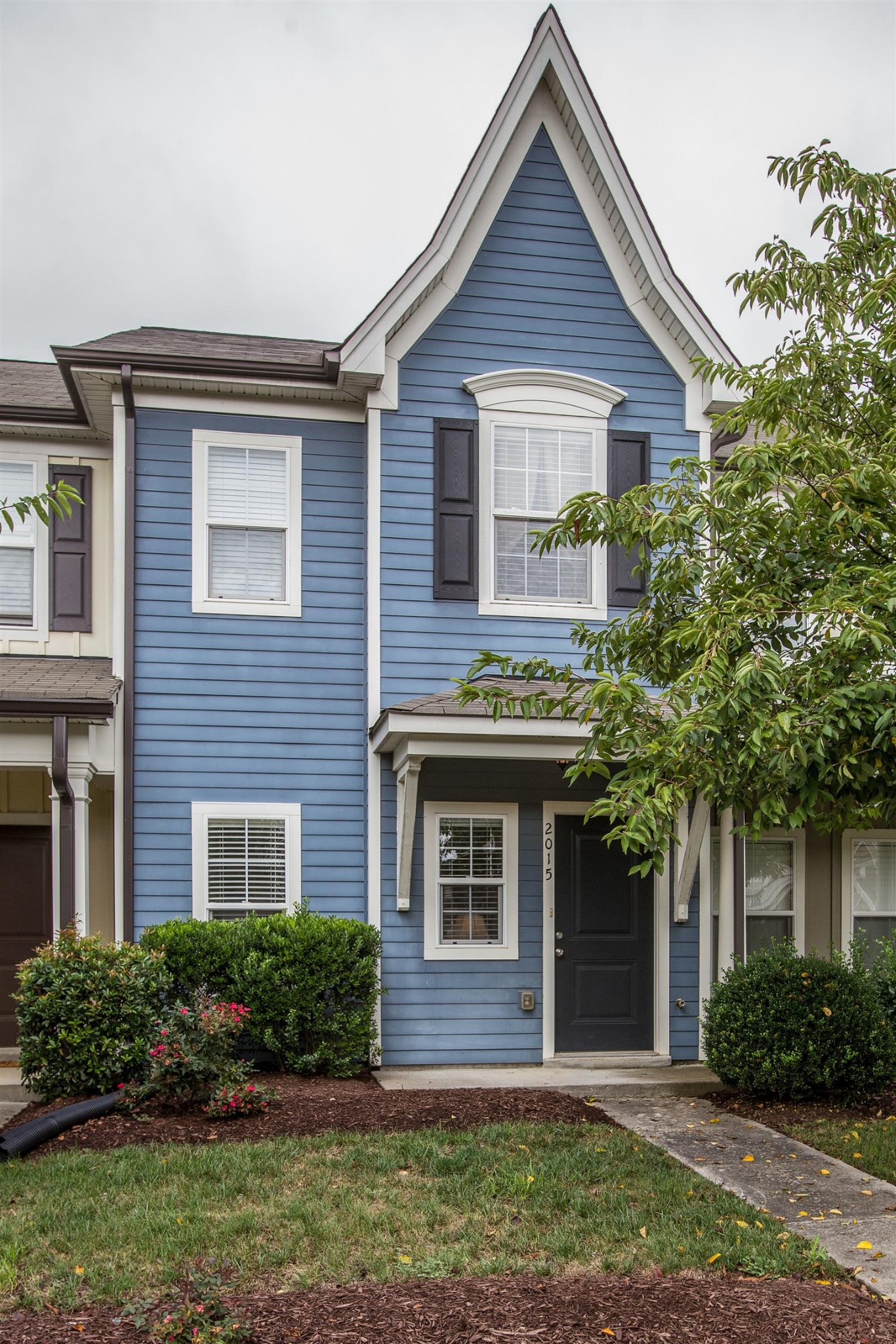 a view of a brick house with a yard plants and large tree