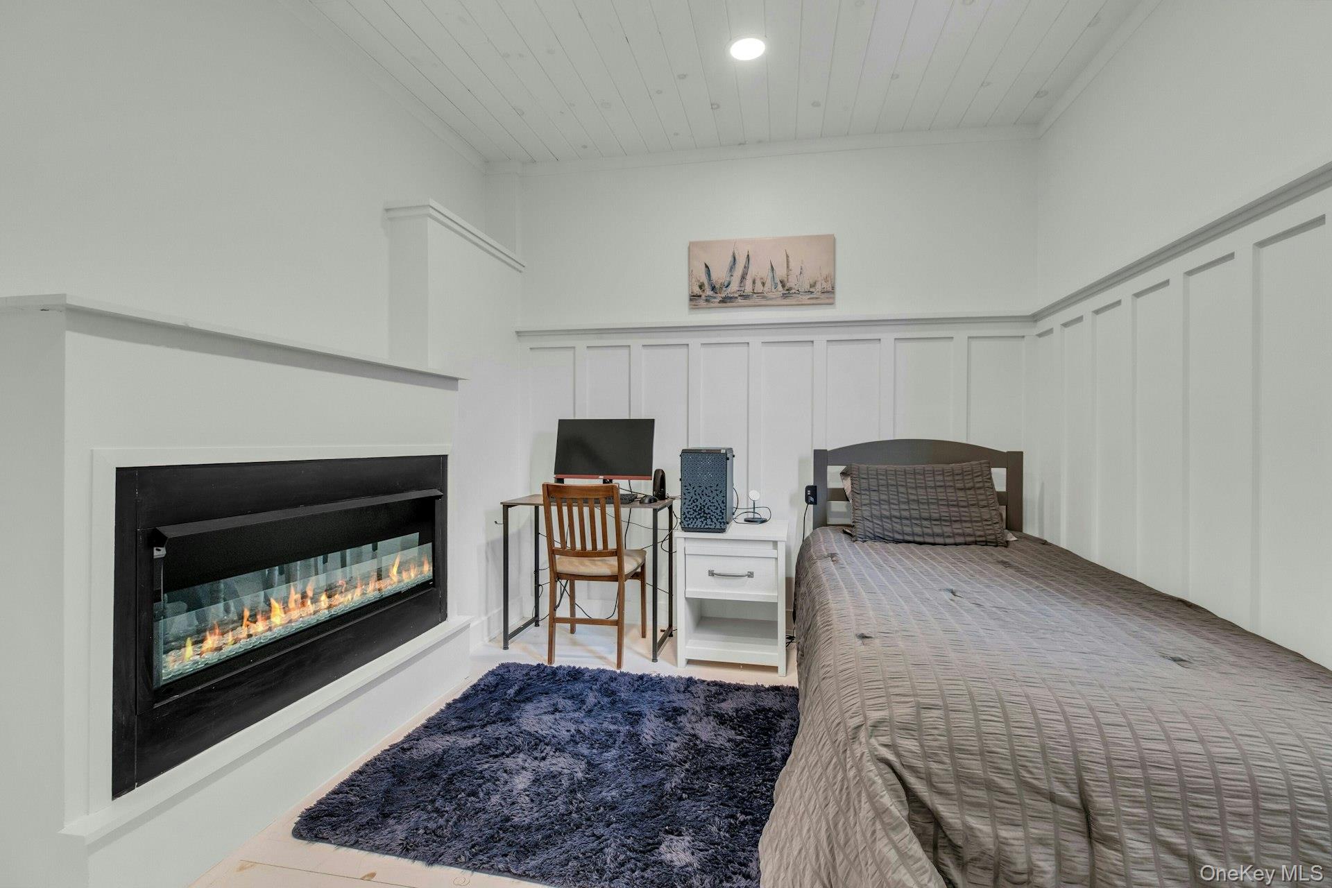 7 Springville Circle Hampton Bays, NY 11946 - Photo 16 of 43 Bedroom featuring a decorative wall, wooden ceiling, a glass covered fireplace, wainscoting, and recessed lighting
