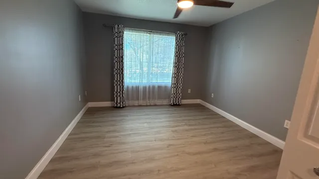an empty room with wooden floor chandelier fan and windows