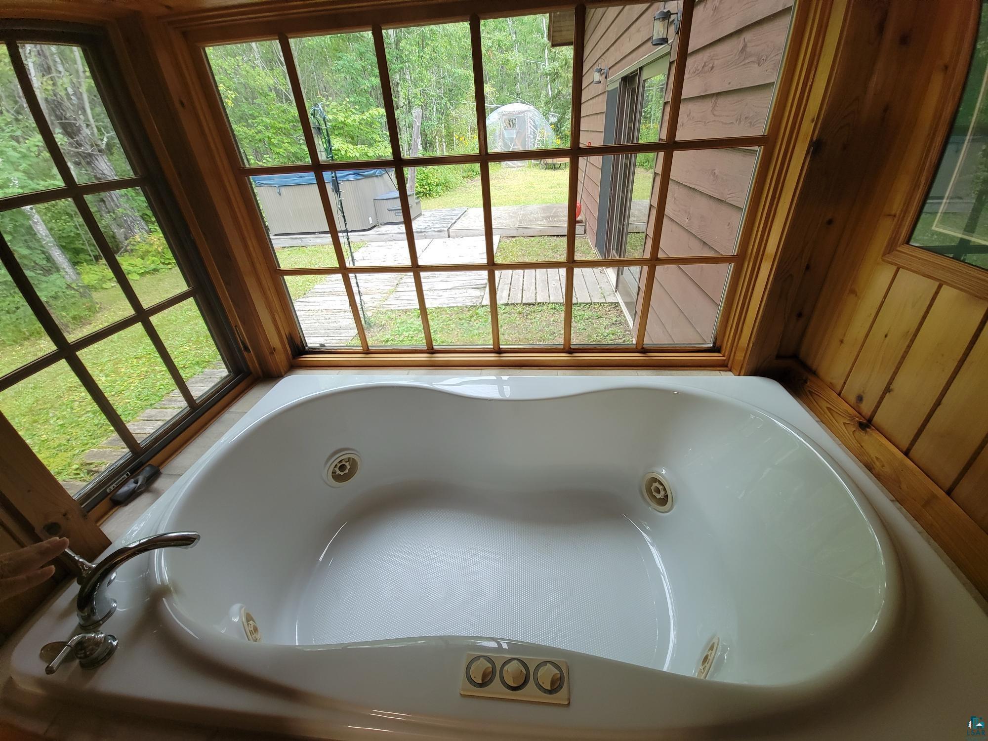 181 Linnell Road Grand Marais, MN 55604 - Photo 48 of 77 Built-in jetted tub with polished chrome fixtures, wood-clad window framing, and wood-paneled walls