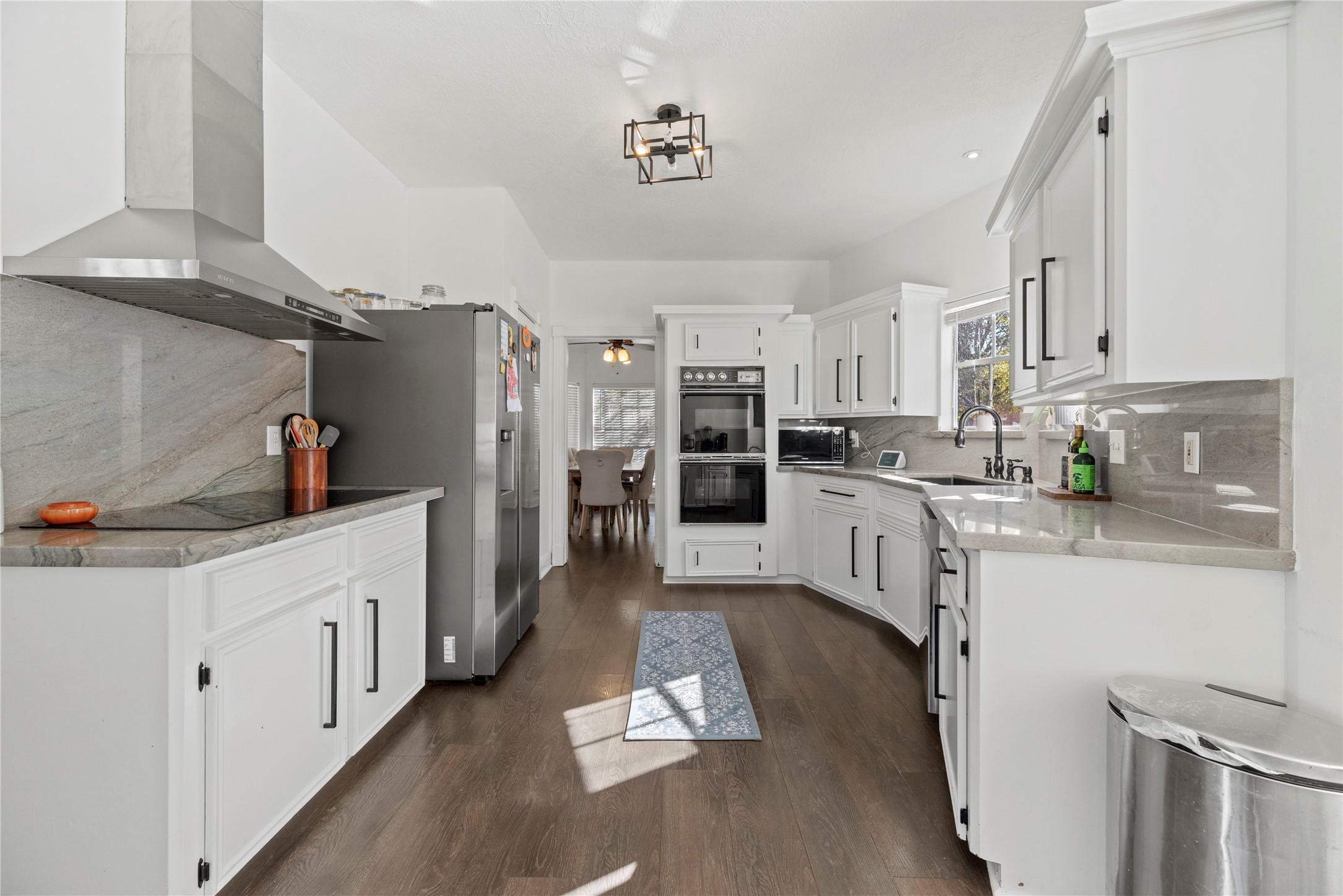14926 Camino Rancho Drive Houston, TX 77083 - Photo 5 of 22 Step into this well-designed kitchen, featuring quartz countertops and stainless steel appliances, including an electric cooktop with a large vent hood above.