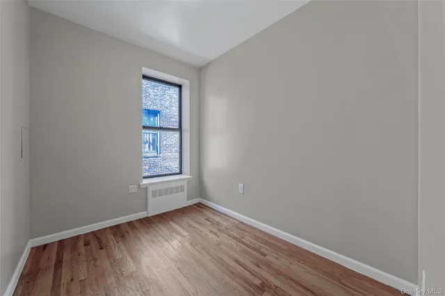 a view of an empty room with wooden floor and window