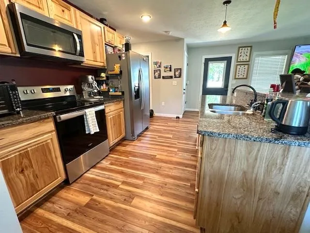 a kitchen with stainless steel appliances granite countertop a refrigerator a stove top oven a sink dishwasher and wooden cabinets with wooden floor