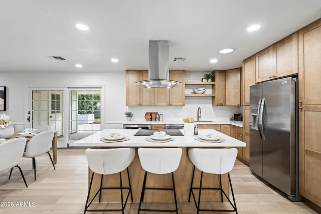 a kitchen with stainless steel appliances granite countertop a dining table chairs refrigerator and wooden cabinets