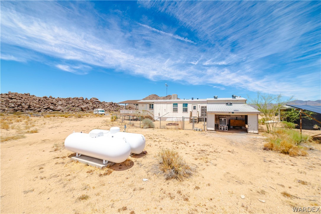 16435 South Wyatt Earp Road Yucca, AZ 86438 - Photo 27 of 57 Desert property featuring a white modular home, attached garage, two large propane tanks, an elevated deck, and solar panels