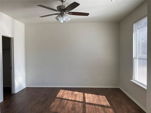 an empty room with wooden floor fan and windows