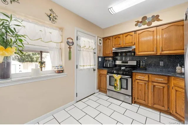a kitchen with stainless steel appliances granite countertop a sink a stove a refrigerator cabinets and a window