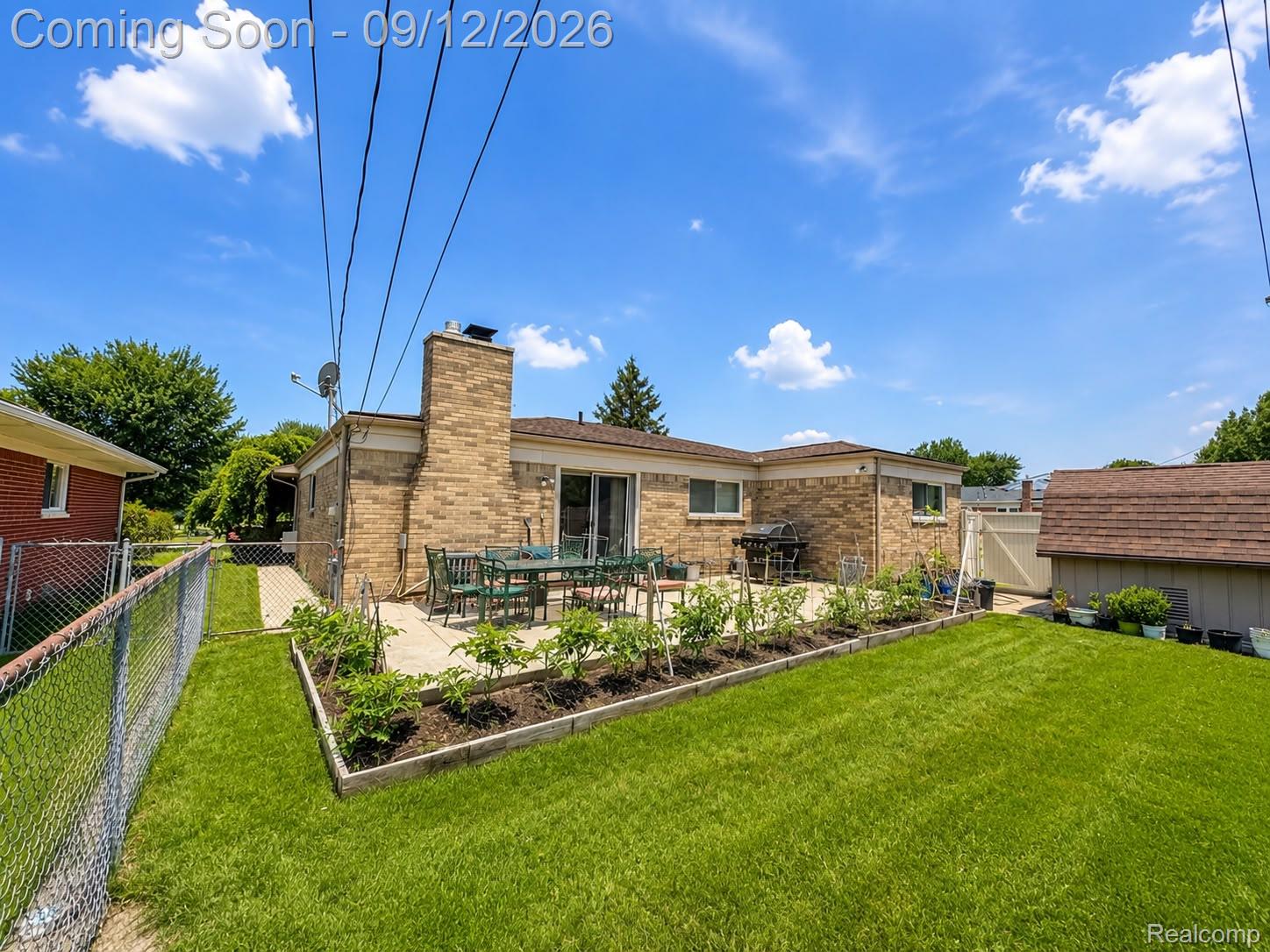 34398 Greentrees Road Sterling Heights, MI 48312 - Photo 31 of 36 Expansive grass yard with a chain-link fence, mature plantings in raised beds, and a patio area