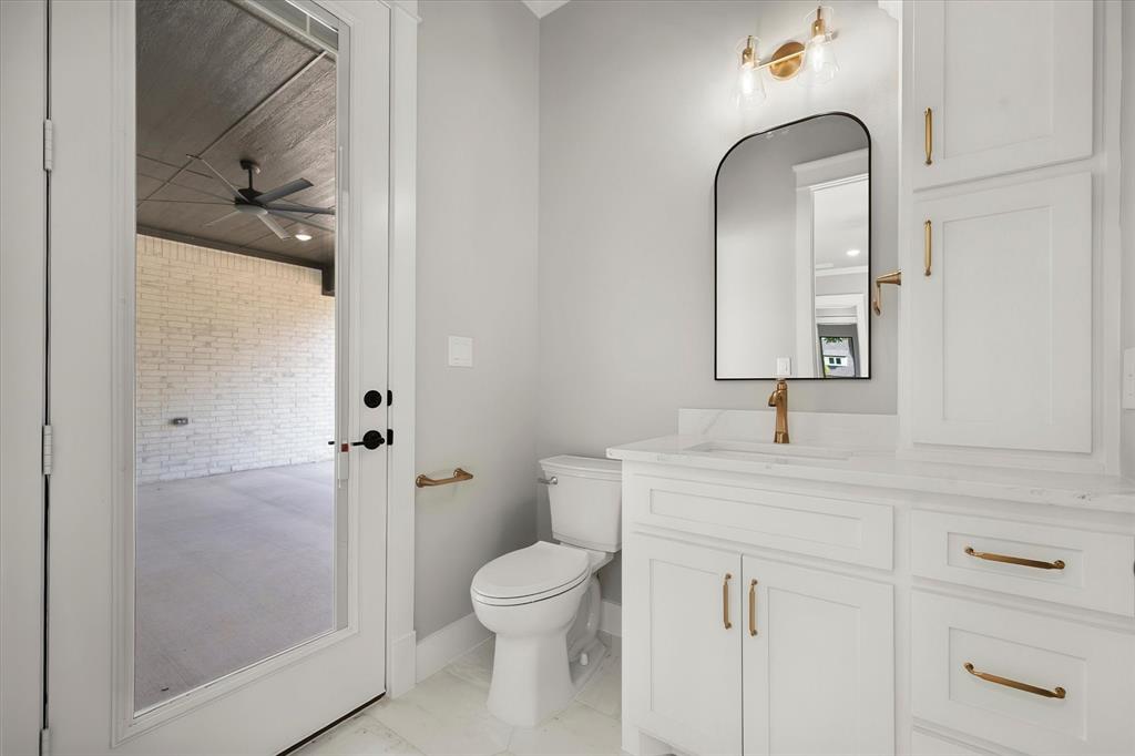 7631 Woodstream Road Midlothian, TX 76065 - Photo 28 of 40 White shaker cabinetry with gold-tone hardware, a white countertop with an integrated sink, a contemporary arched mirror, and a gold-tone wall sconce