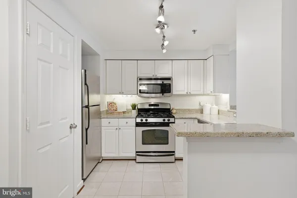 a kitchen with stainless steel appliances granite countertop a refrigerator a stove a sink and white cabinets
