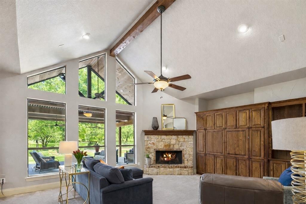 1520 Snider Court Lucas, TX 75002 - Photo 4 of 40 The spacious living room features floor-to-ceiling windows that flood the space with natural light while overlooking the wooded backyard, a gorgeous stone fireplace, stained wood built-ins, and a vaulted ceiling with an exposed beam.