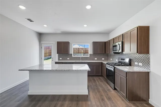 a large white kitchen with stainless steel appliances granite countertop a stove a sink dishwasher and a microwave with wooden floor