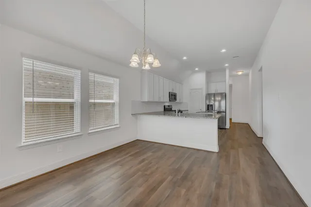 a view of an empty room with kitchen and window