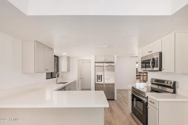 a kitchen with stainless steel appliances a stove top oven a sink a refrigerator white cabinets and wooden floor