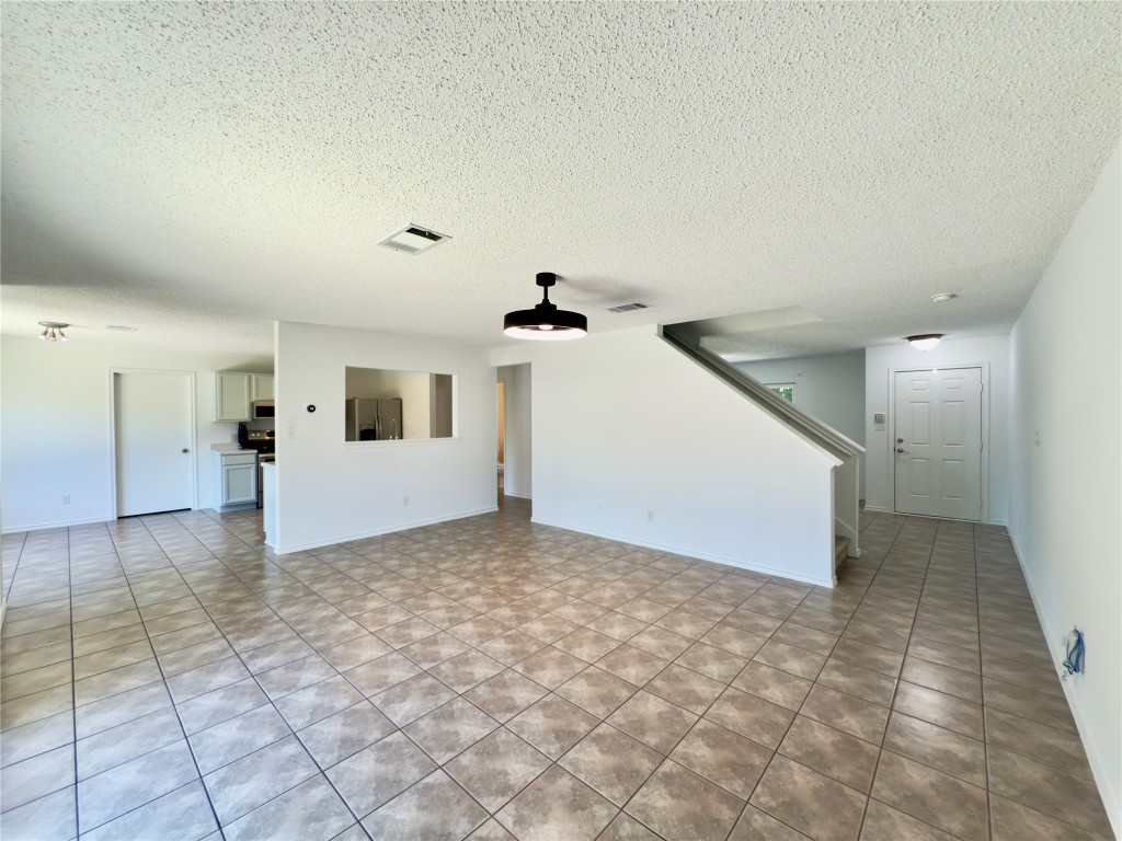 7817 Marble Ridge Drive Austin, TX 78747 - Photo 12 of 38 Unfurnished living room featuring a textured ceiling, stairs, light tile patterned floors, and baseboards
