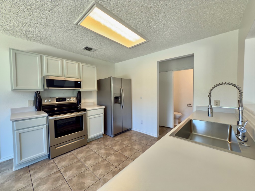 7817 Marble Ridge Drive Austin, TX 78747 - Photo 16 of 38 Kitchen with appliances with stainless steel finishes, a sink, a textured ceiling, light countertops, and light tile patterned floors