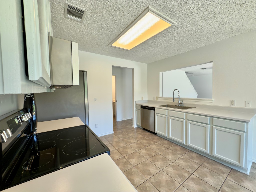 7817 Marble Ridge Drive Austin, TX 78747 - Photo 17 of 38 Kitchen with stainless steel appliances, a sink, light countertops, a textured ceiling, and light tile patterned flooring