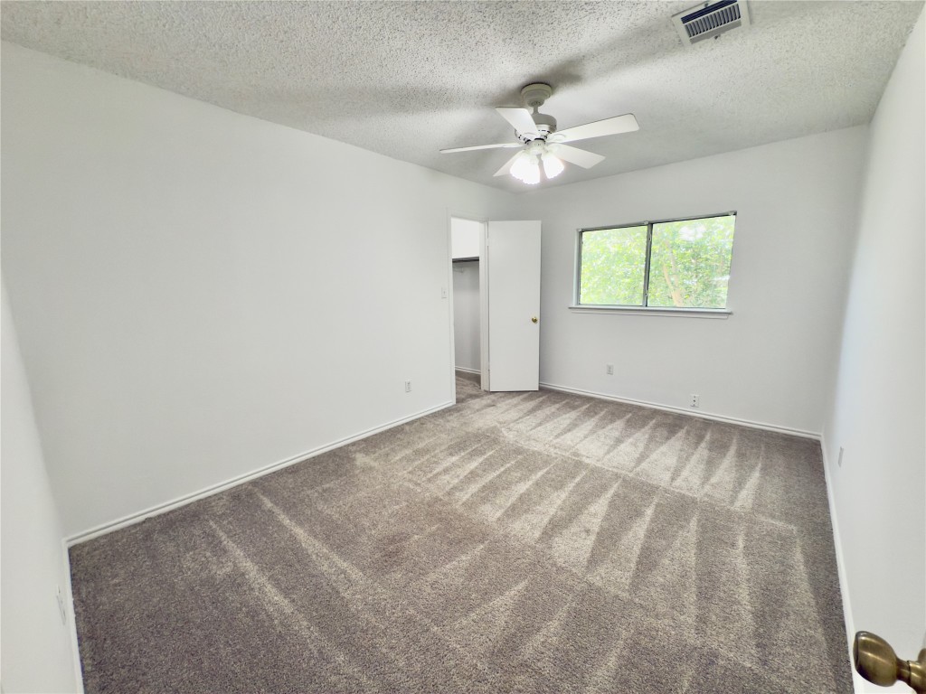 7817 Marble Ridge Drive Austin, TX 78747 - Photo 26 of 38 Unfurnished bedroom featuring carpet, a textured ceiling, baseboards, a spacious closet, and a ceiling fan
